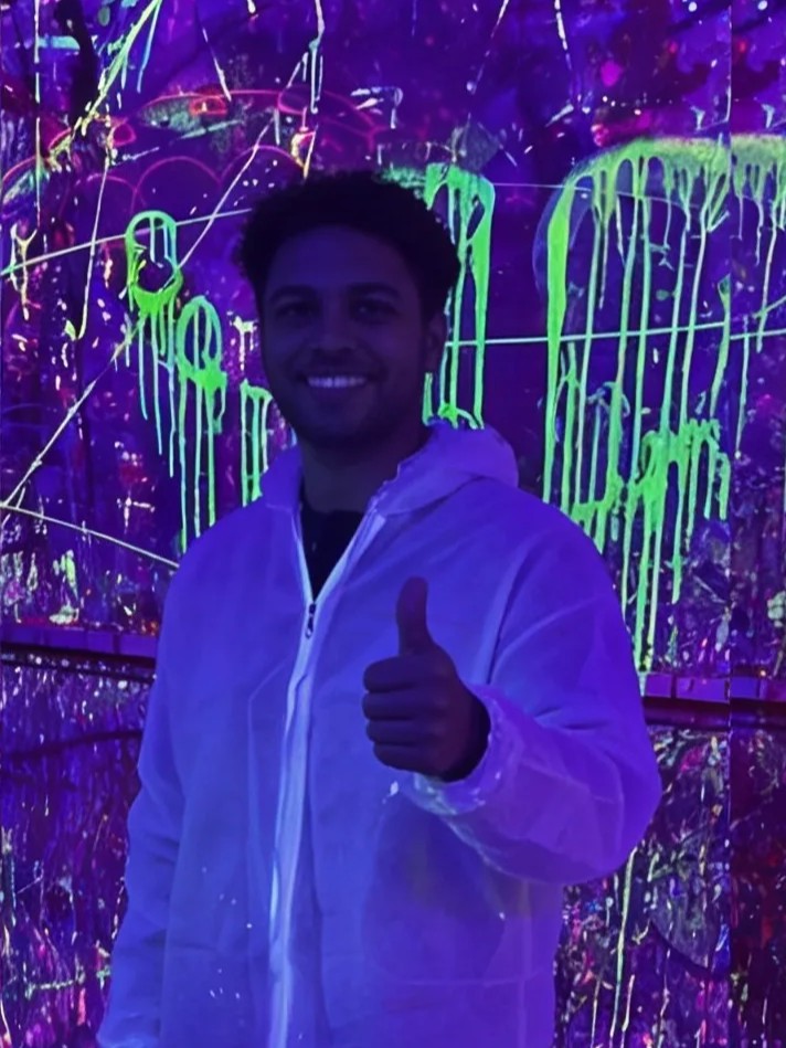Cliente con mono blanco haciendo el gesto de pulgar arriba en la Splatter Room bajo luz UV